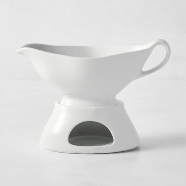 A classic-shaped white porcelain sauce boat on a hollow white porcelain stand with a cutout for placing a tealight candle