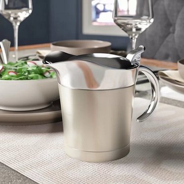A tall stainless steel gravy boat with a hinged lid