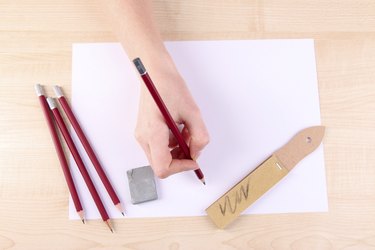Hand holding pencil with art materials on wooden background
