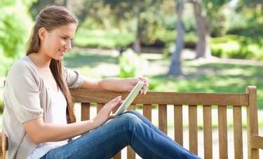 Side view of a woman using a tablet computer on a park bench