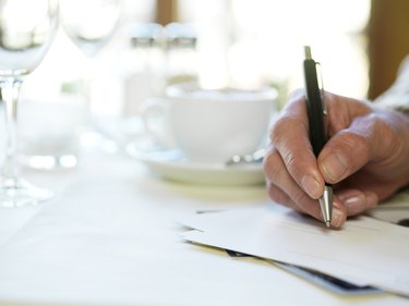 Man in restaurant, holding pen to paper, close-up of hand