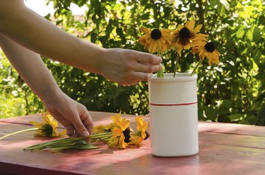Woman hands put rudbekia flowers in white vase