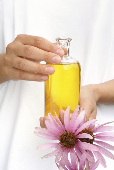 Hands of young woman holding essential oil and fresh coneflowers