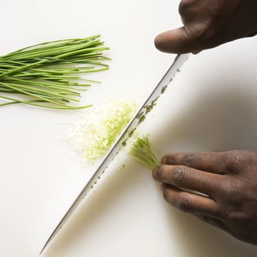 African-American male hands using large kitchen knife to chop fresh chives.