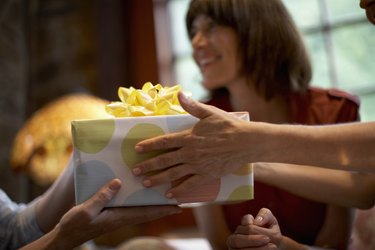 Two women exchanging gift over table, close-up of hands, out of focus woman in background