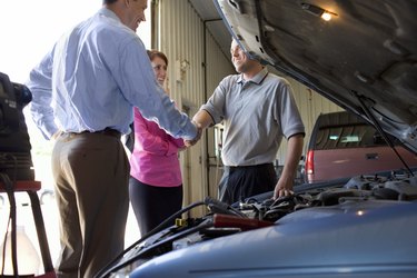 Couple shaking hands with auto mechanic