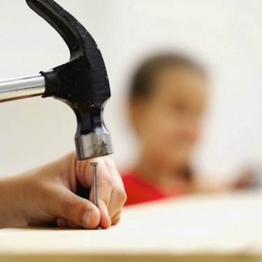 Close-up of the hands of a young boy (8-10) hammering a nail into wood