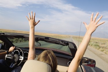 Woman in convertible with arms raised