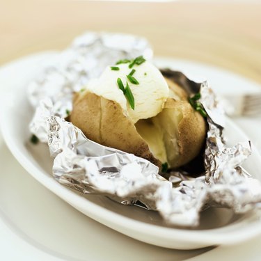 close-up of a baked potato served with sour cream in foil