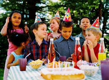 Group of children (4-10) standing in front of a table with cake and snacks celebrating a birthday