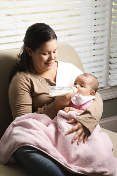 Woman washing baby bottle nipples under stream of water, above