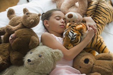 Hispanic girl sleeping in bed surrounded by stuffed animals