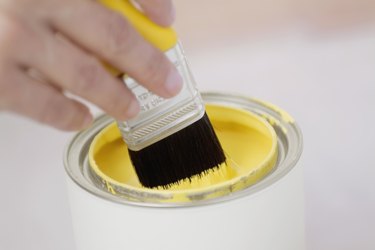 Human hand holding a paint brush over a paint can