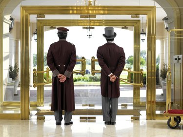 Concierge and bellboy standing at hotel entrance, rear view