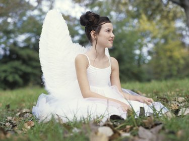 Girl (9-11) sitting on grass wearing angel costume, side view