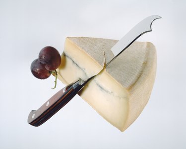 Slice of cheese, grape and knife on white background, close-up 