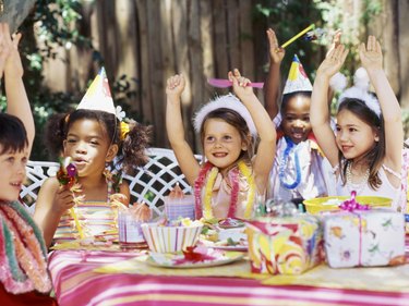 Group of children sitting at a table at a birthday party with their arms raised