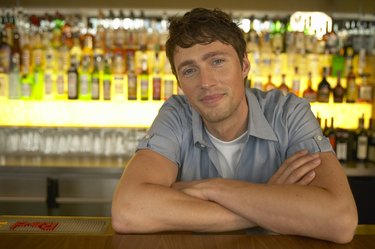 Man working in bar, leaning on bar with folded arms, portrait