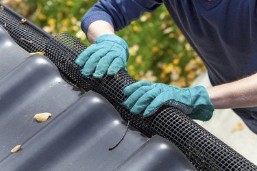 Man's hands in gloves securing gutters with a black net