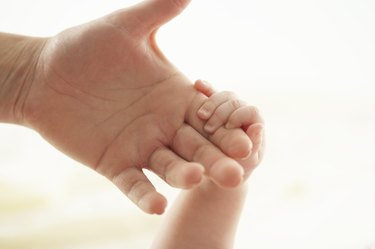 Baby girl (3-6 months) holding woman's hand, close-up