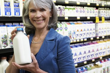 Mature woman holding bottle of milk in supermarket, portrait, close-up