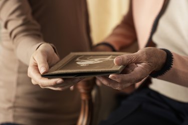 Senior woman and young woman holding old photograph, mid section, close-up of hands