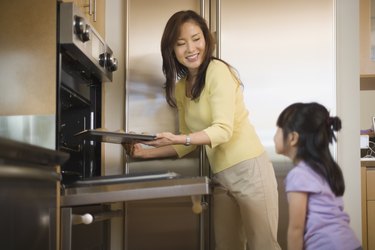Mother putting cookies into oven with daughter