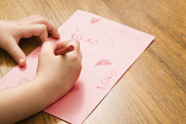 Caucasian female child hands drawing on paper with crayons.