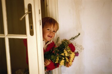 Boy (4-5) with bunch of flowers at door, smiling