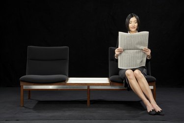 Businesswoman sitting on bench reading newspaper, smiling