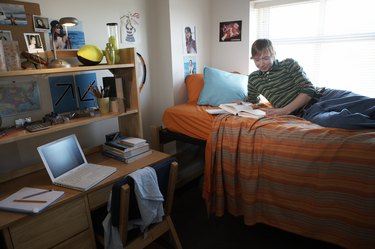 Young man reading on bed in dorm room, smiling, side view