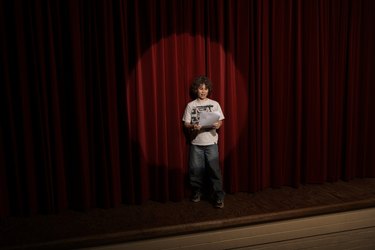 Spotlight on boy (10-12)  standing on stage, reading lines