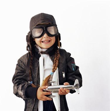 Girl (3-5) wearing goggles holding toy aeroplane, smiling, portrait