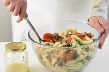 Mixing pasta salad in a glass bowl, close up