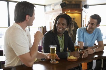 "Three men drinking at bar, smiling"