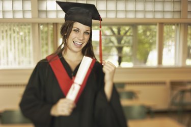 Excited teenage girl wearing cap and gown holding diploma