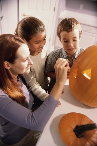 Mother carving a pumpkin with her son and daughter