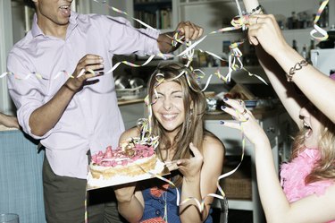 Friends throwing streamers over woman holding cake