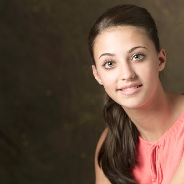 portrait of a cute ethnic teenage girl in a pink shirt with long brown hair as she smiles