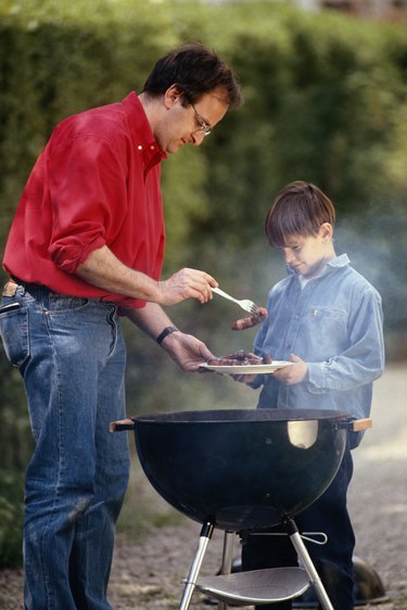 Father serving cooked food in son's (6-9) plate, outdoors