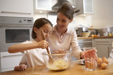 Mother and daughter (6-8) baking in kitchen, smiling