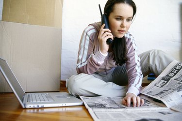 Woman on floor multitasking with laptop, phone and newspaper
