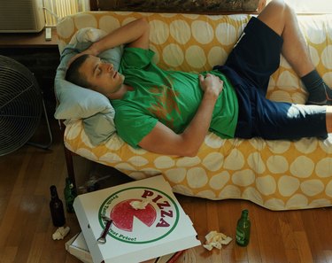 Man lying on sofa, discarded take-away boxes and beer bottles on floor