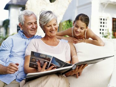 Grandparents and granddaughter (12-14) looking at photo album, smiling