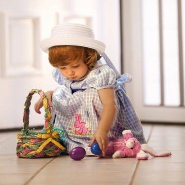 A toddler in her Easter dress plays with eggs in her basket