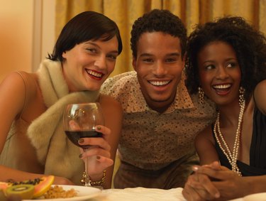 Portrait of a Man Sitting With Two Women in Evening Wear at a Dining Table, Smiling at the Camera