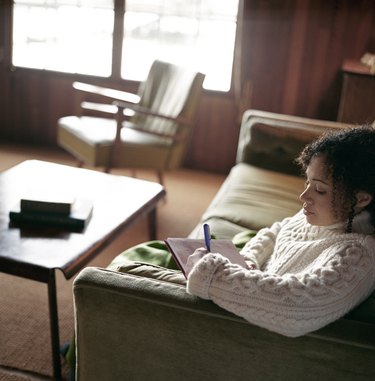 Young woman sitting on sofa, writing letter