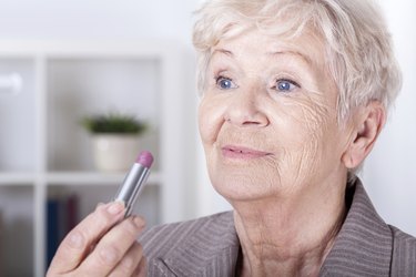 Elderly woman putting on lipstick