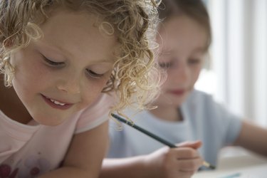 "Two girls (4-6) drawing pictures, one smiling, close-up"