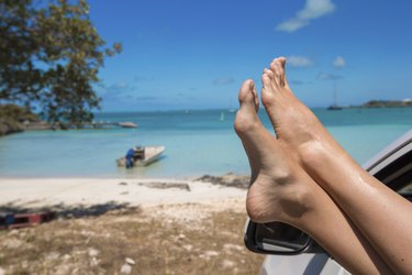 Female feet from window of car on background tropical beach